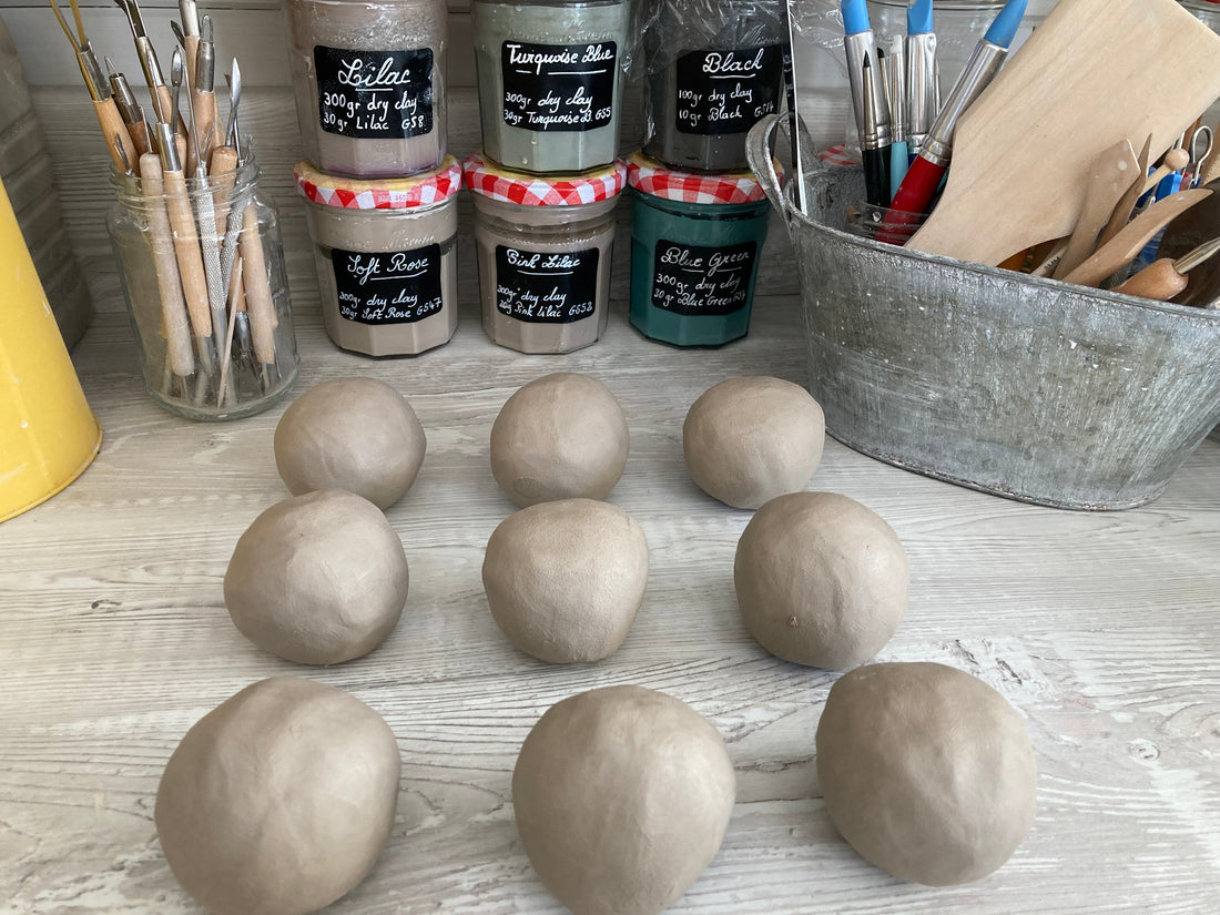 9 balls of fresh clay are neatly set on the studio's worktop ready for the start of a ceramics workshop. Tools are tidied up in a galvanised tub and there are several jam jars containing different colour slips. Private ceramics workshop in Dorset.