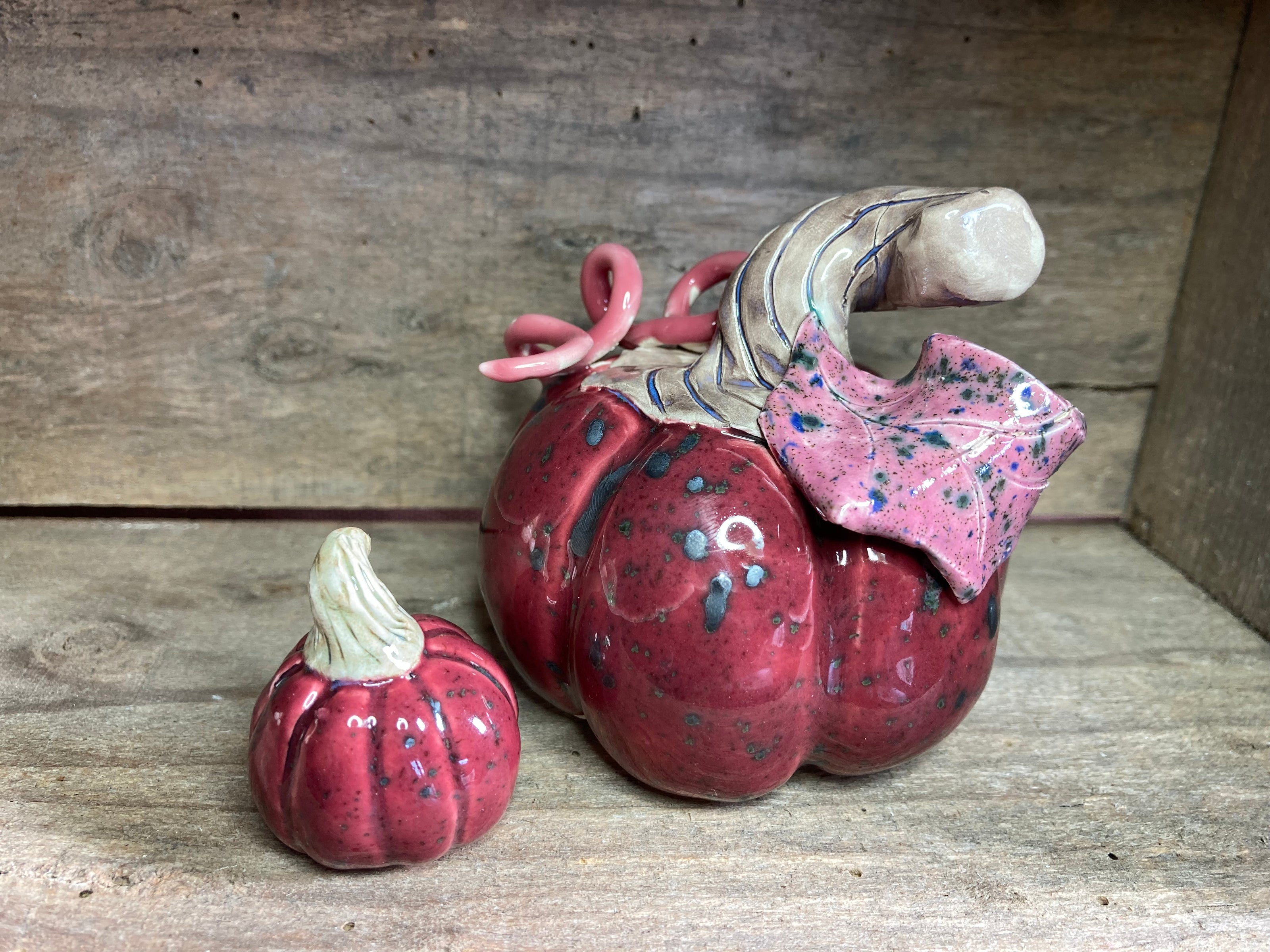 Two cerise colour ceramic pumpkins with textured surface on a wooden background