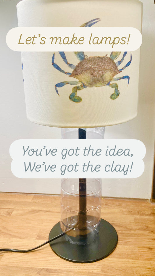 A picture of a table lamp made of a recycled transparent plastic water bottle and a beautiful white lampshade decorated with a watercolour picture of a green and blue crab. 