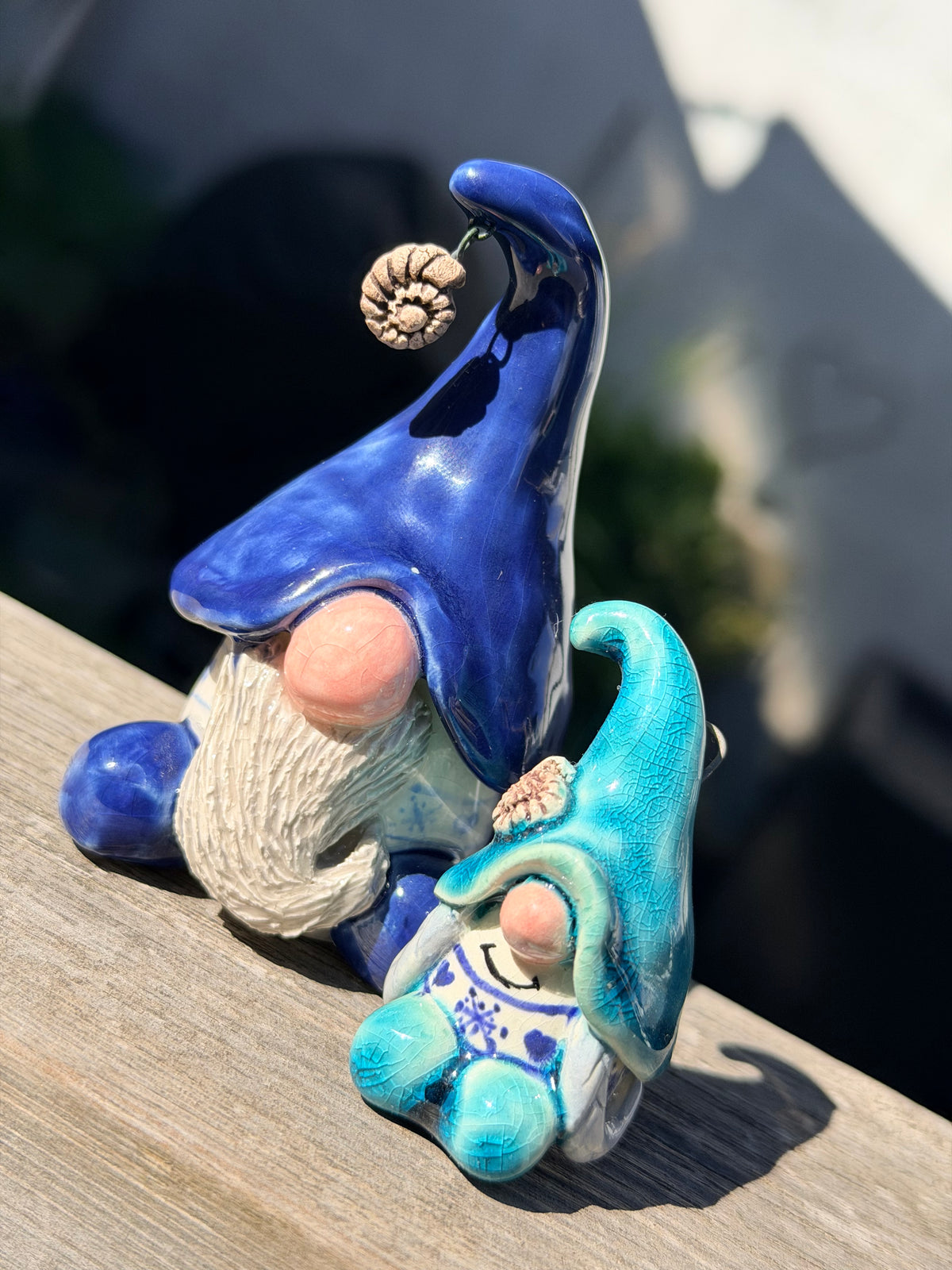 Two cute small Christmas gonks with blue hats that fall over their faces, pink round noses, knitted jumpers with snow flakes and ammonite details. 