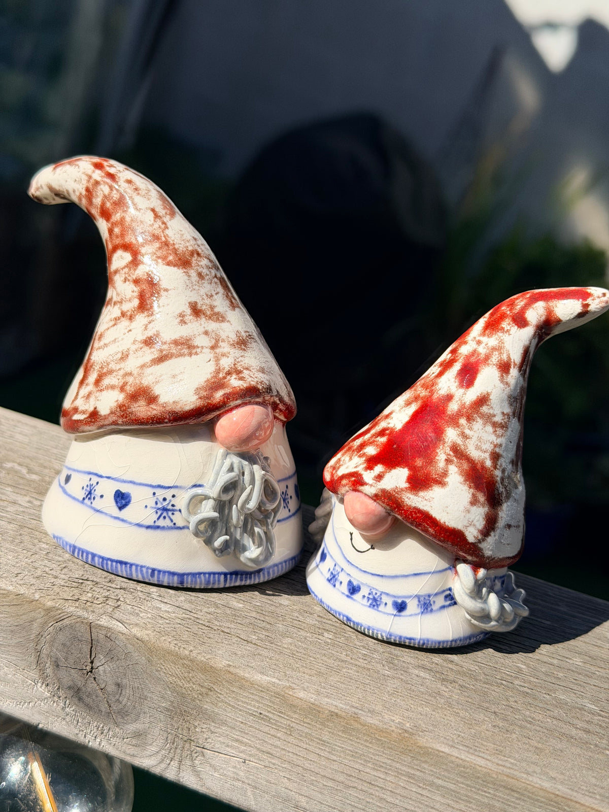 A pair of Mr and Mrs ceramic gonks with oversized hats, pink noses and knitted jumpers. He has a long grey beard and her hair is tied into plats either side of her face.