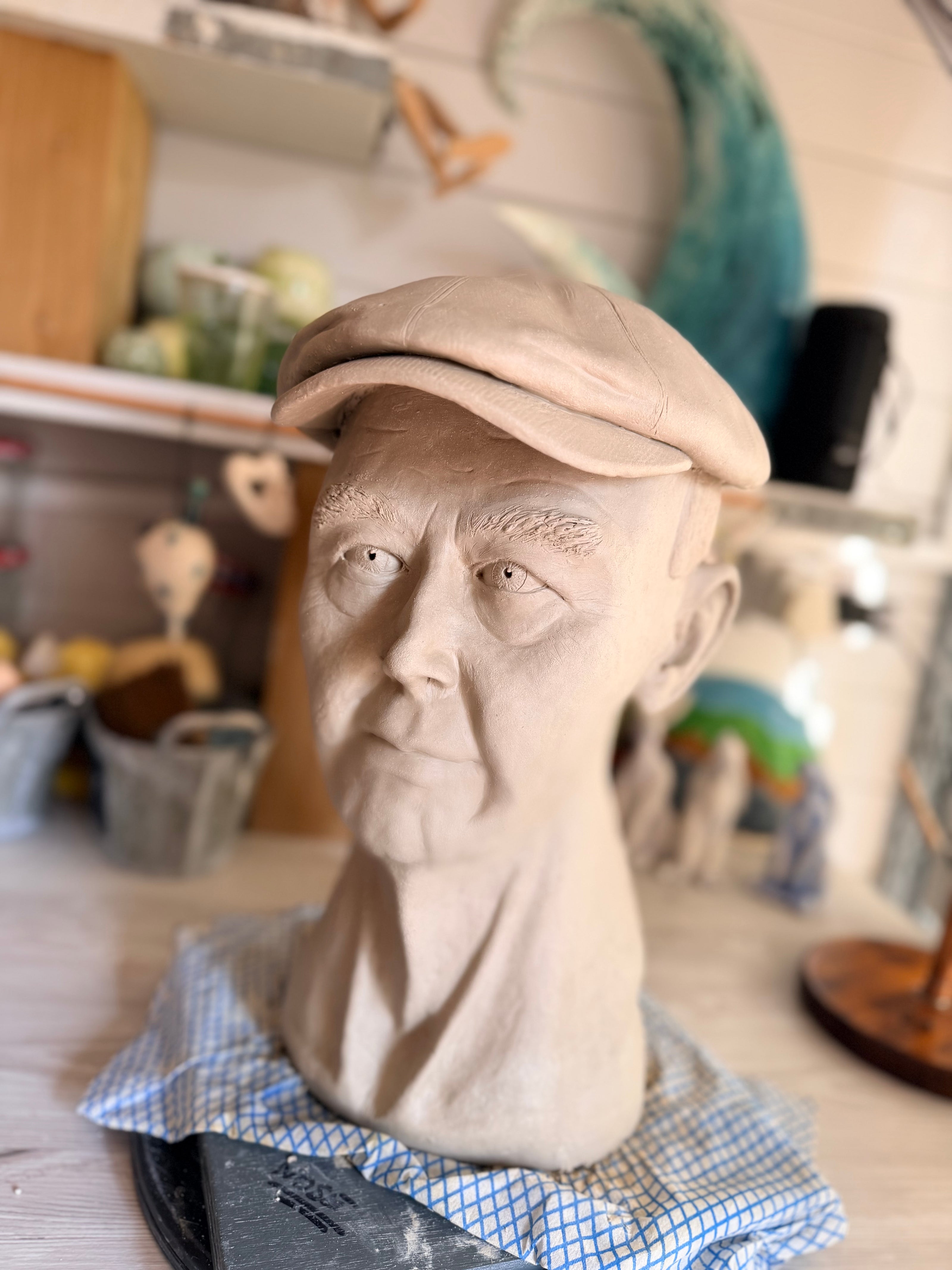 An amazingly lifelike sculpted clay portrait of an elderly man wearing a flat cap, sculpted by blind sculptress Shani with the help of her apprentice. Grandad’s portrait.