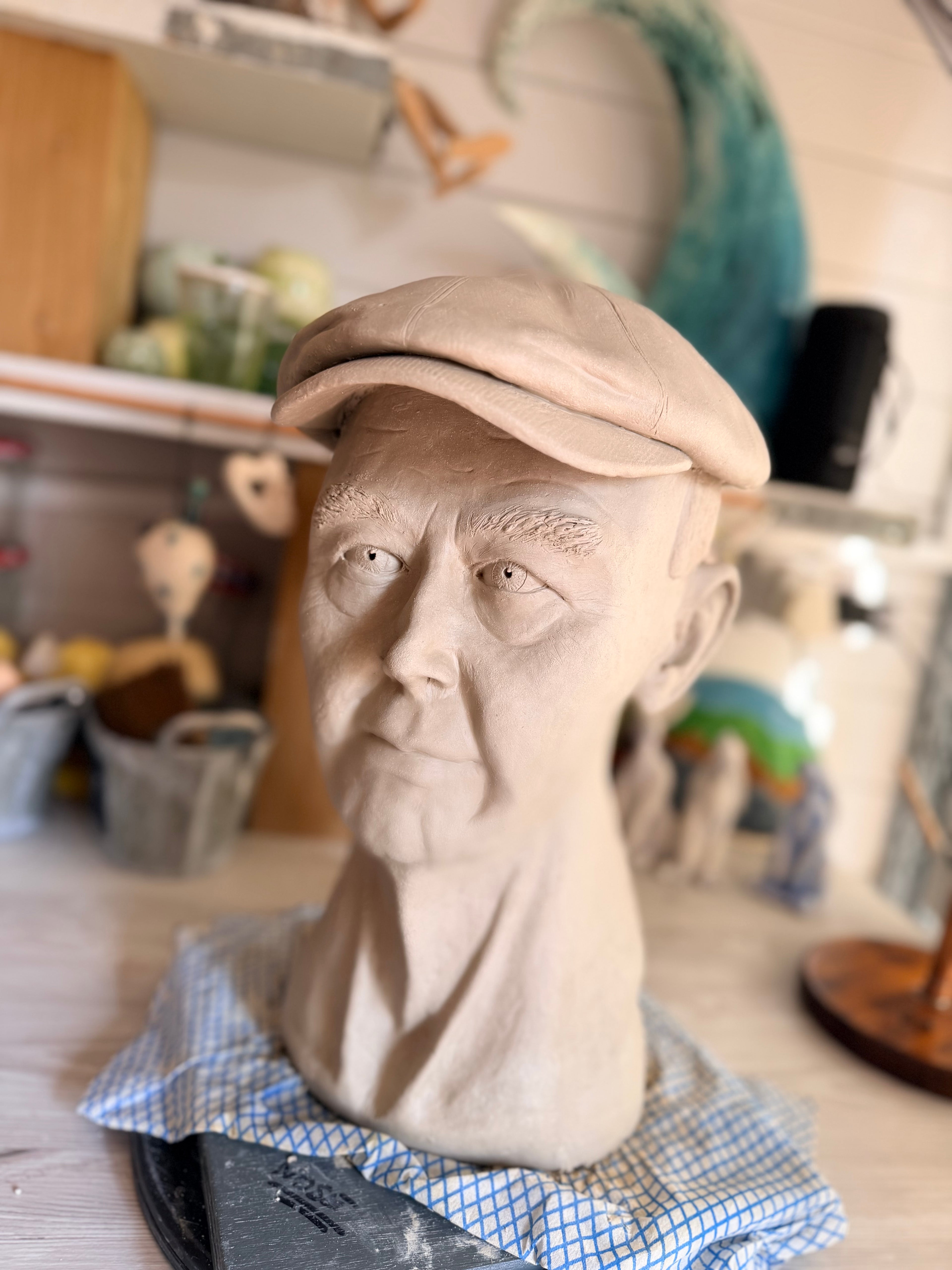 An amazingly lifelike sculpted clay portrait of an elderly man wearing a flat cap, sculpted by blind sculptress Shani with the help of her apprentice. Grandad’s portrait.