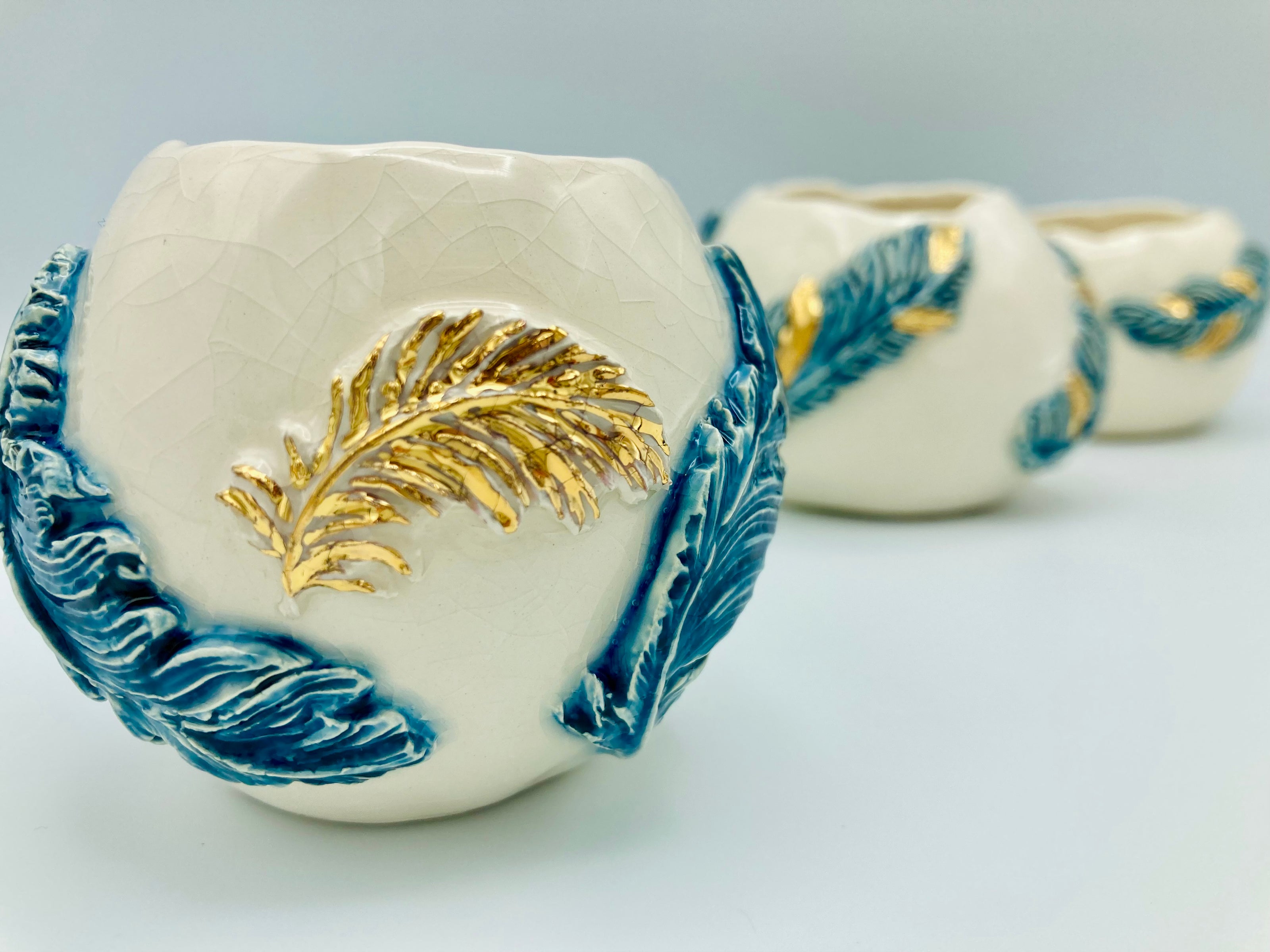3 small round Ceramic pots with gold and blue feathers designs.