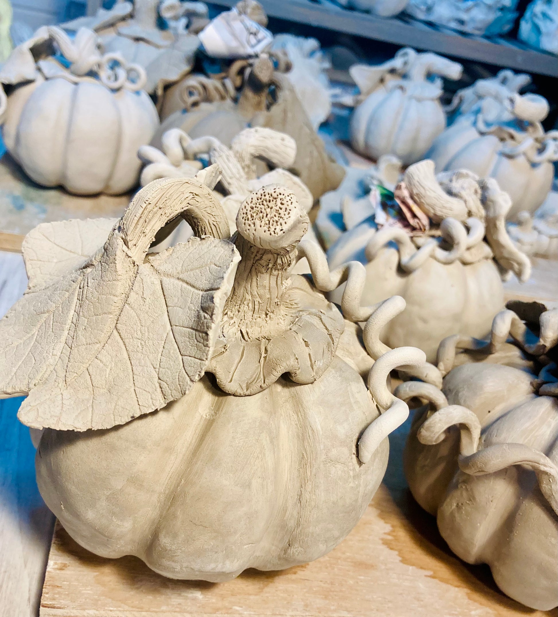 Decorative ceramic pumpkins with detailed features on a wooden surface. They are all pale grey as they have just been made and show the colour of the clay before it is fired in the kiln