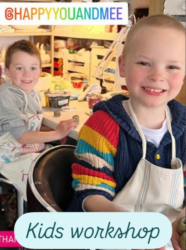 Two smiling children in a ceramics studio, participating in a kids workshop.